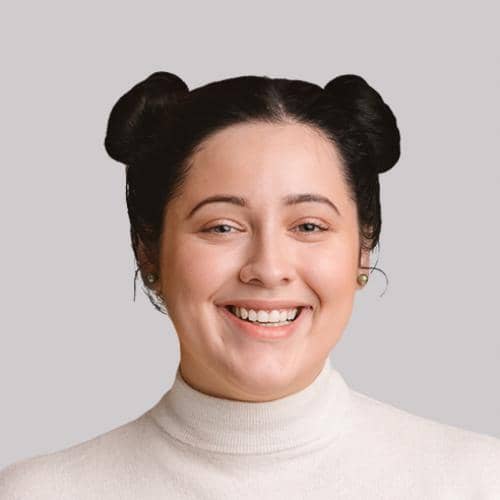 SOMA Fit Club A woman with dark hair styled in two buns is smiling. She is wearing a white turtleneck sweater and pearl earrings, posed against a plain gray background, ready for her 20 Minute workout inspired by EMS Canada. EMS Training