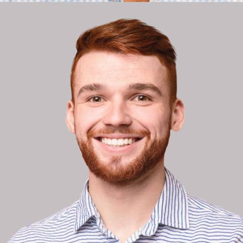 SOMA Fit Club A young man with short red hair and a beard, smiling, wearing a light blue and white striped shirt against a plain gray background—ready for his next EMS workout at SOMA Fit Club. EMS Training